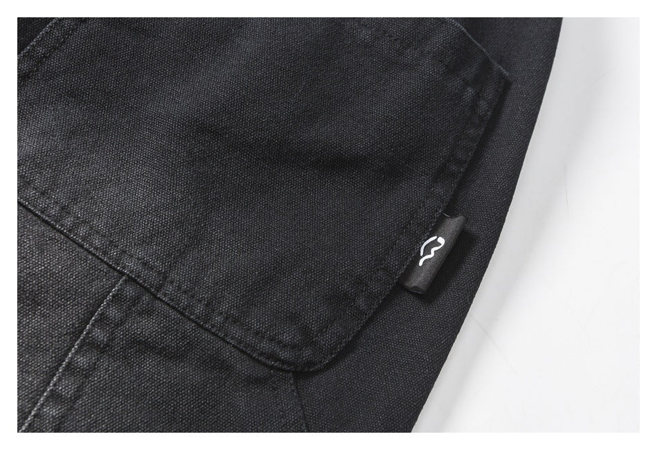 Close-up of a stitched pocket on black trousers with a small white symbol on a fabric side tab.