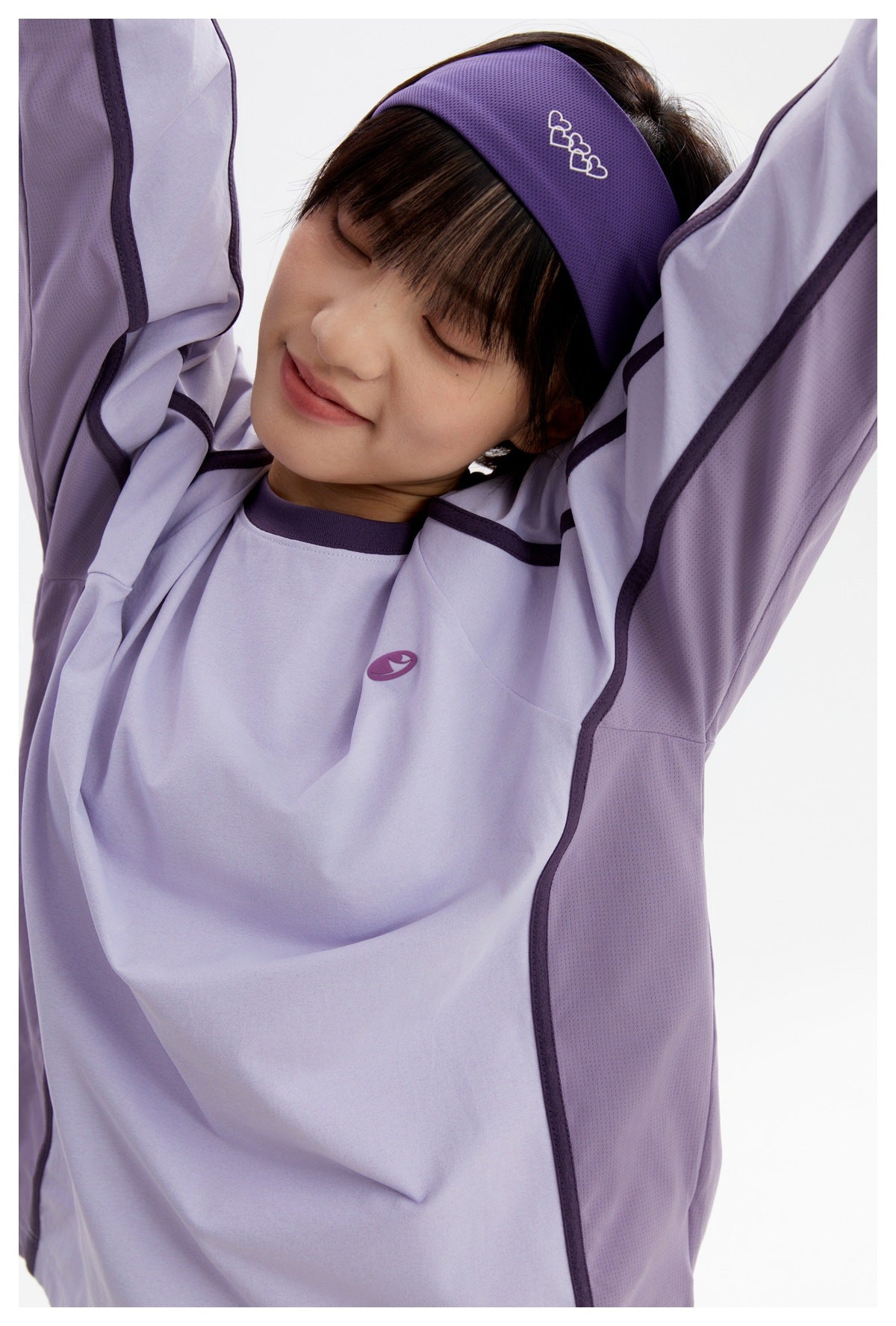 Close-up of a model wearing a lavender top with dark purple piping and a purple headband with white heart outlines.