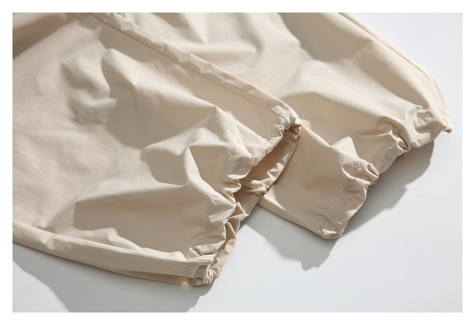Close-up of gathered elastic hems on cream pants, laid flat.