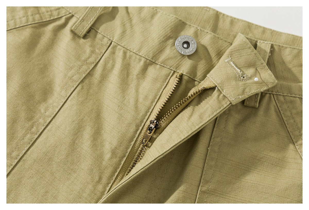 Close-up of the khaki shorts' waistband, metal button, and partially open zipper fly.