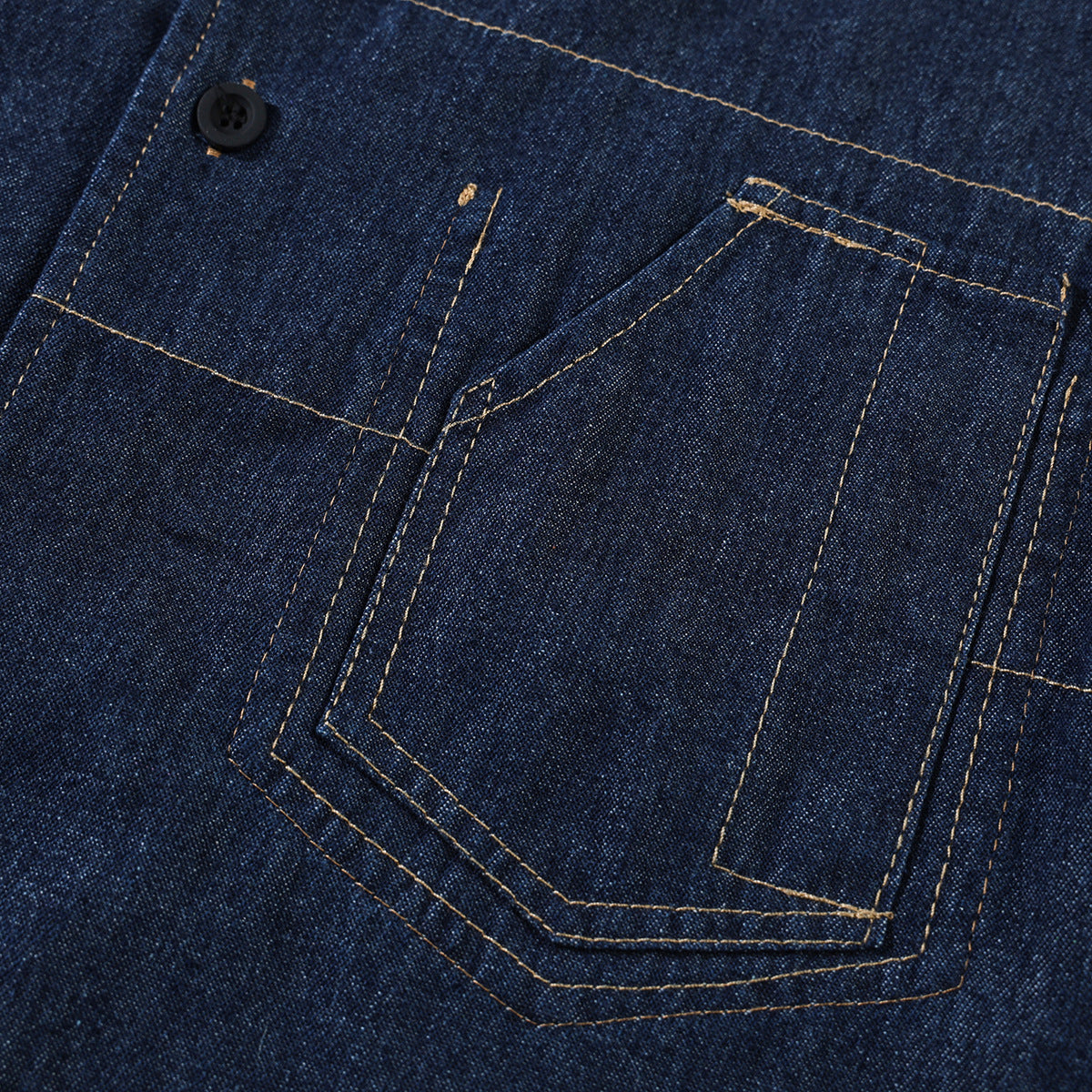 Close-up of a dark indigo denim shirt pocket with tan contrast stitching and a black button.
