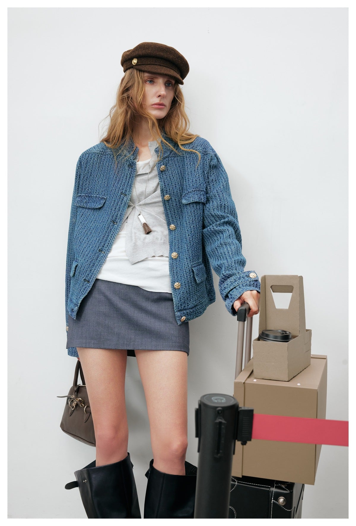 Model wearing a blue textured jacket with gold buttons and flap pockets, paired with a white top and gray mini skirt.