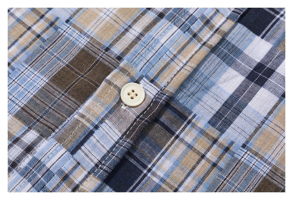 Close-up of a cream four-hole button on a blue, navy, brown, and white plaid shirt.