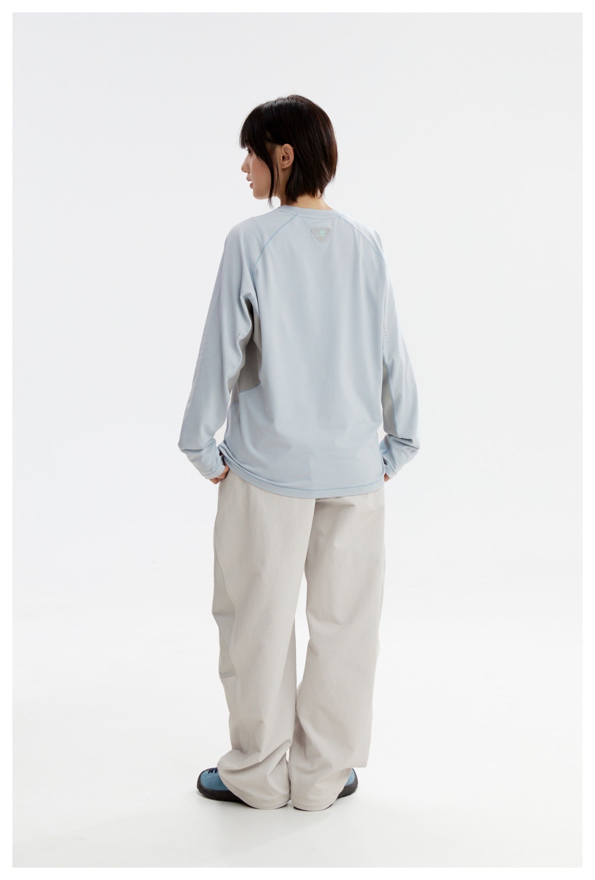 Rear view of a model wearing a pale blue long-sleeve shirt with gray side panels and white trousers.