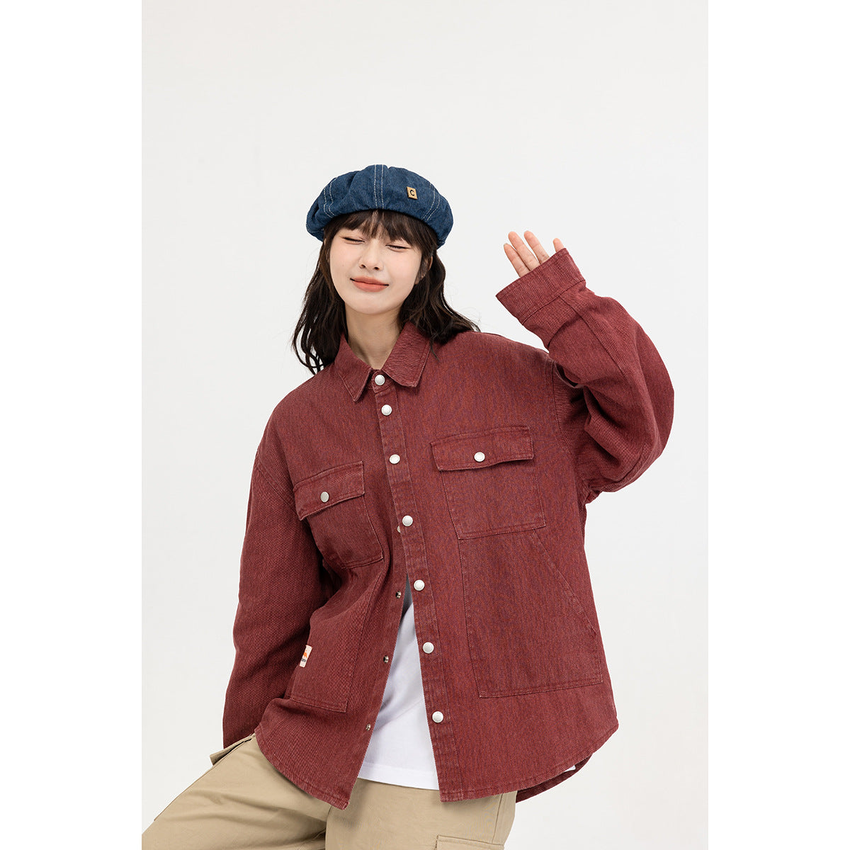 Model wearing a muted red button-up overshirt with flap chest pockets over a white tee and beige trousers.