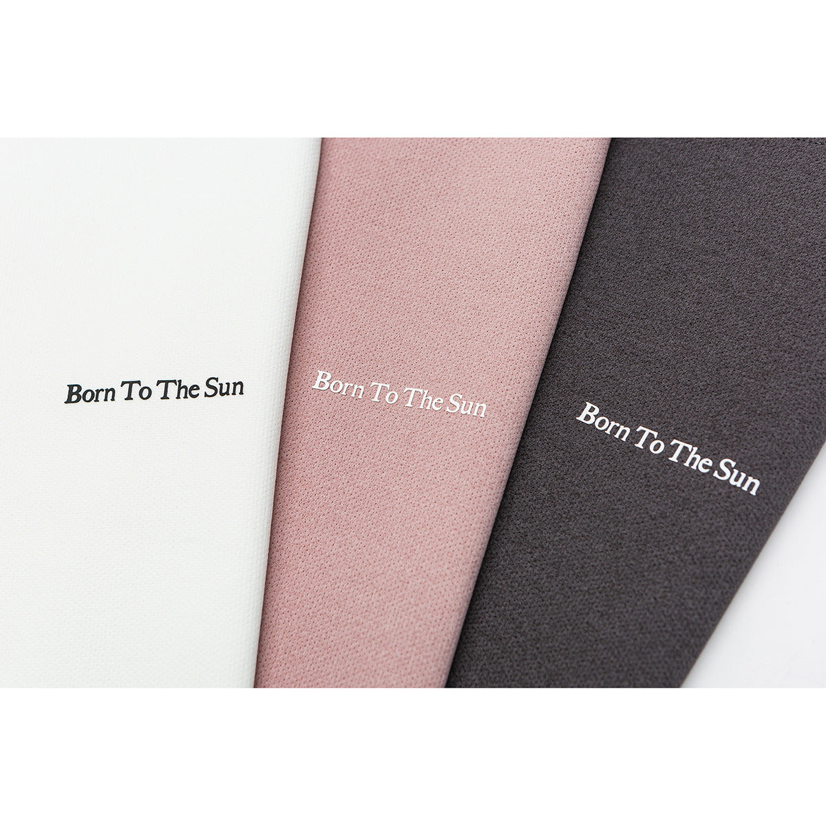Close-up of white, dusty pink, and charcoal fabric panels, each printed with “Born To The Sun.”