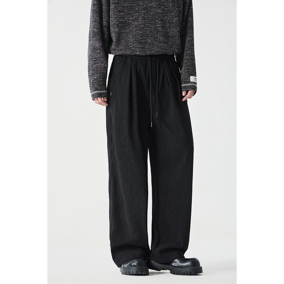 Front view of black wide-leg drawstring pants with a subtle crinkled texture, worn with a dark sweater.