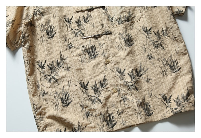 Close view of a beige short-sleeve shirt with dark botanical print, front buttons and metal bar fasteners.