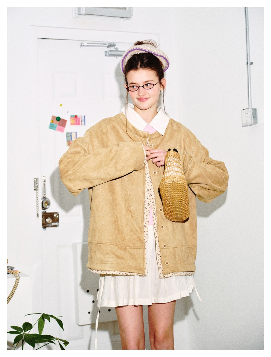 Model holding a woven bag while wearing an oversized tan jacket with floral trim and a white skirt.