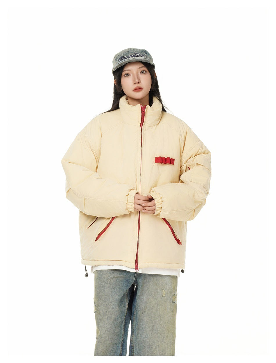 Model wearing a cream padded jacket with a high collar, red zipper and pocket accents, and wide jeans.