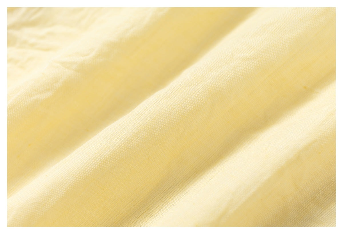 Extreme close-up of the pale yellow shirt's fine woven fabric and softly crinkled surface.