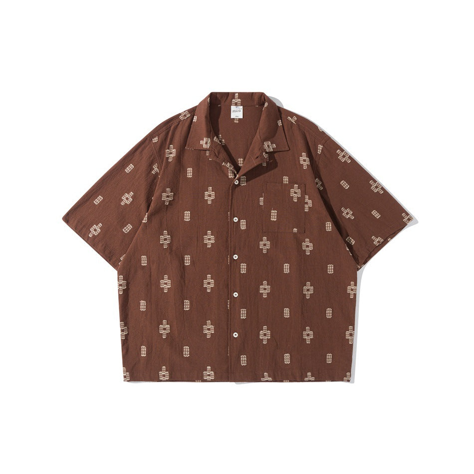 Brown short-sleeve camp-collar shirt with cream cross and rectangle motif, chest pocket and buttons, flat lay