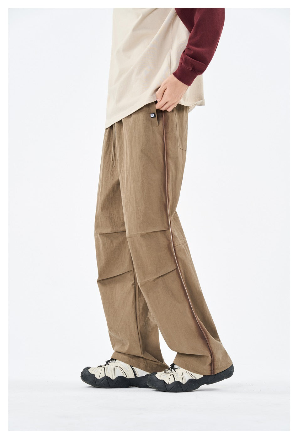 Side view of a model wearing loose khaki pants with contrast piping and paneled legs.