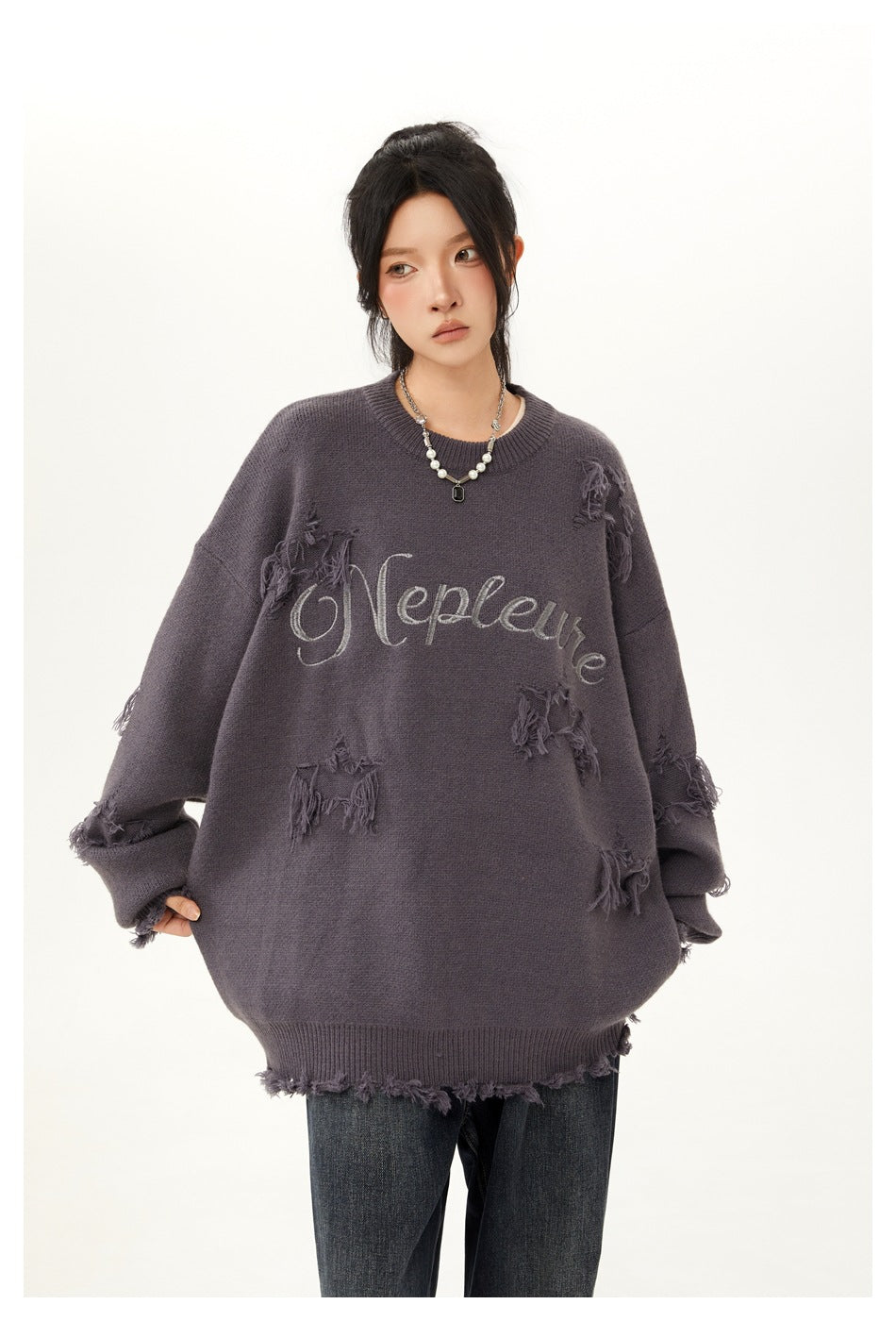 Model wearing an oversized charcoal-gray sweater with script lettering and distressed patches, paired with dark jeans.