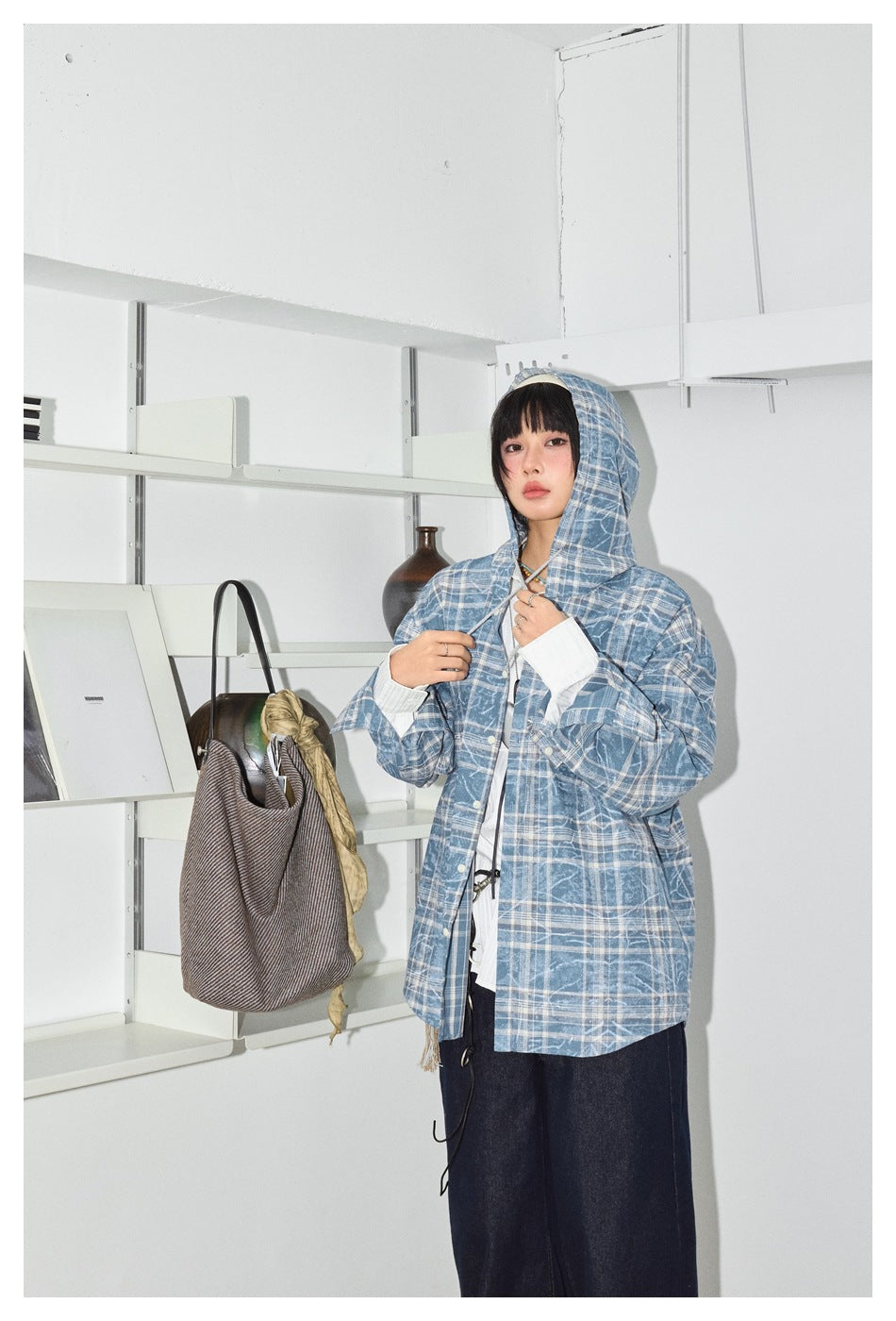 Model wearing a blue-and-white plaid hooded jacket over a white blouse, shown from the front with the hood up.