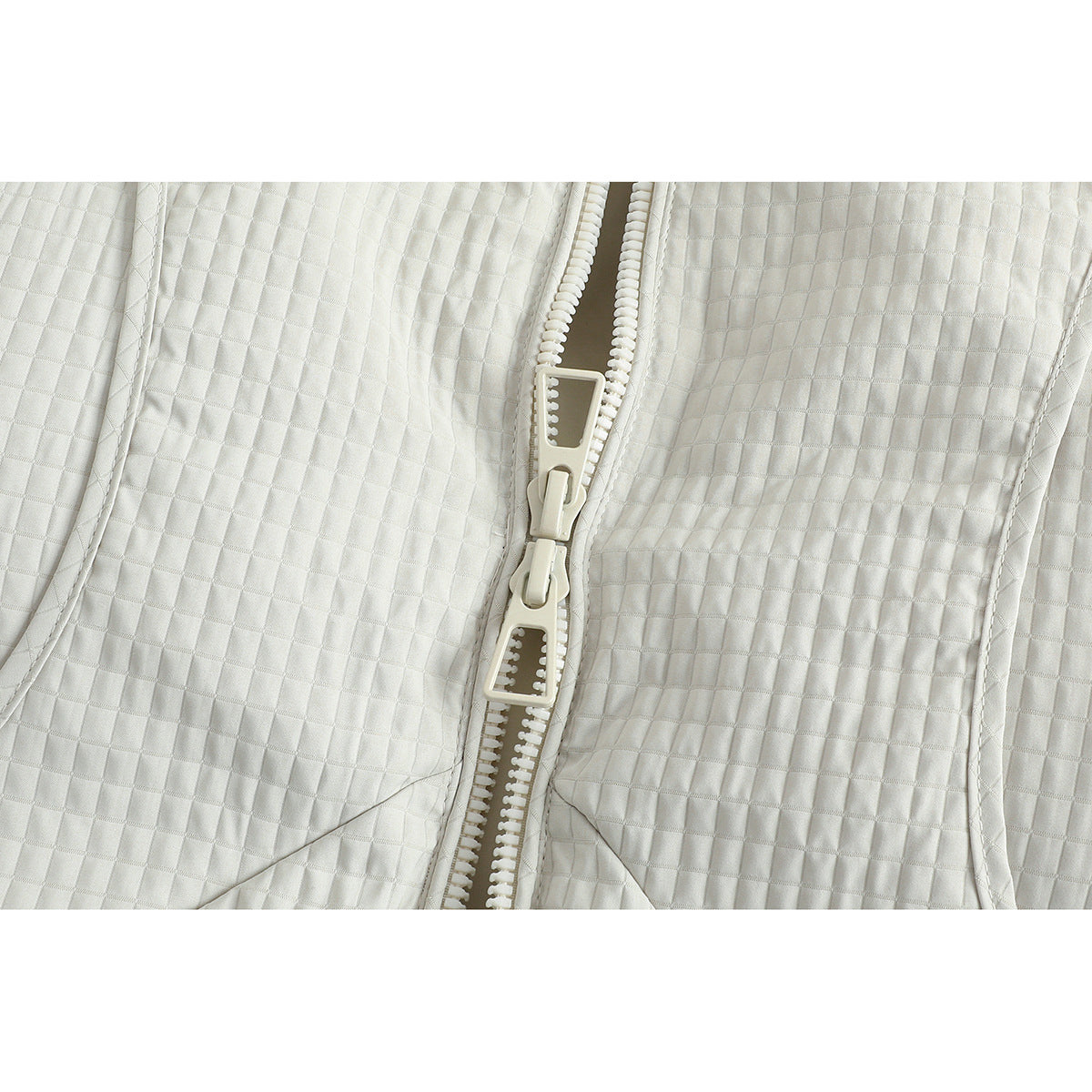 Close-up of the ivory jacket's chunky double zipper and square quilted texture.