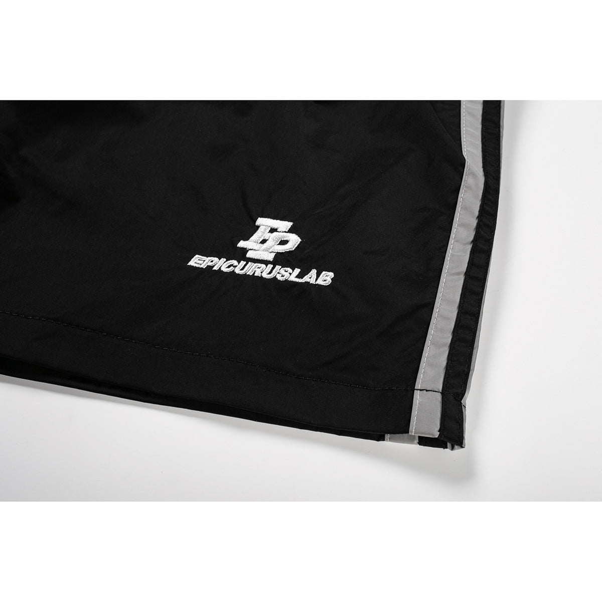Close-up of black shorts with a white embroidered logo and a gray side stripe.