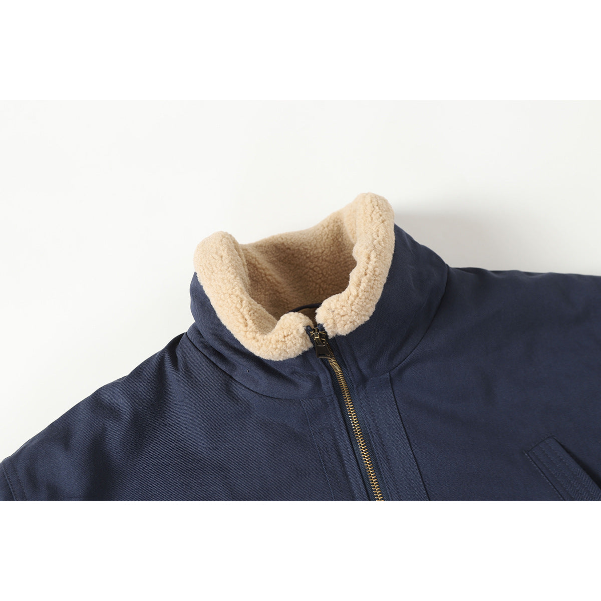 Close-up of a navy jacket with a cream sherpa-lined collar and brass front zipper.