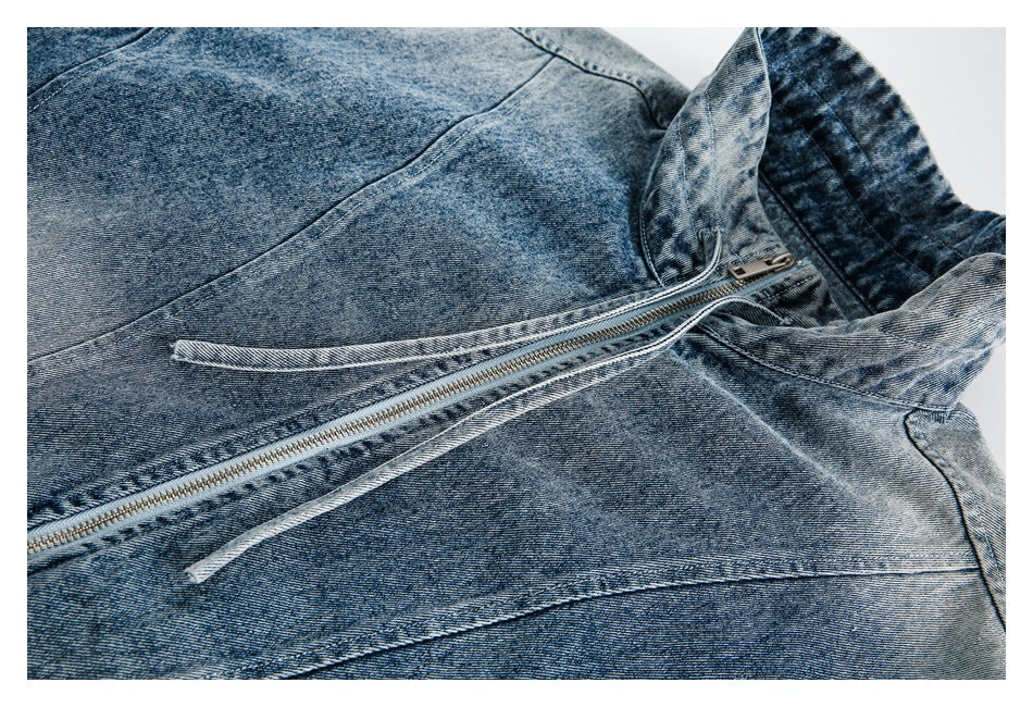 Close-up of the washed denim jacket's diagonal front zipper, tie detail and panel seams.