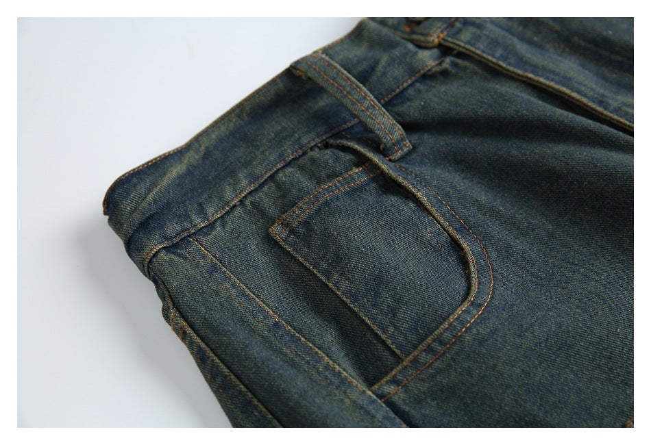 Close-up of a front pocket and belt loop on dark indigo jeans with orange contrast stitching.