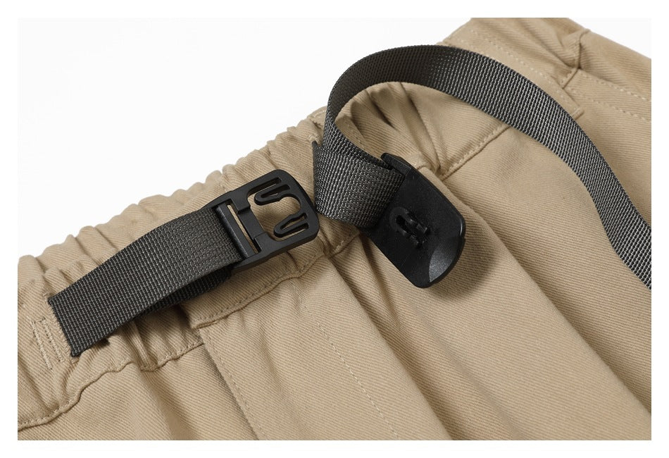 Close-up of the tan pants' dark webbing belt and plastic buckle fastening at the elastic waistband.