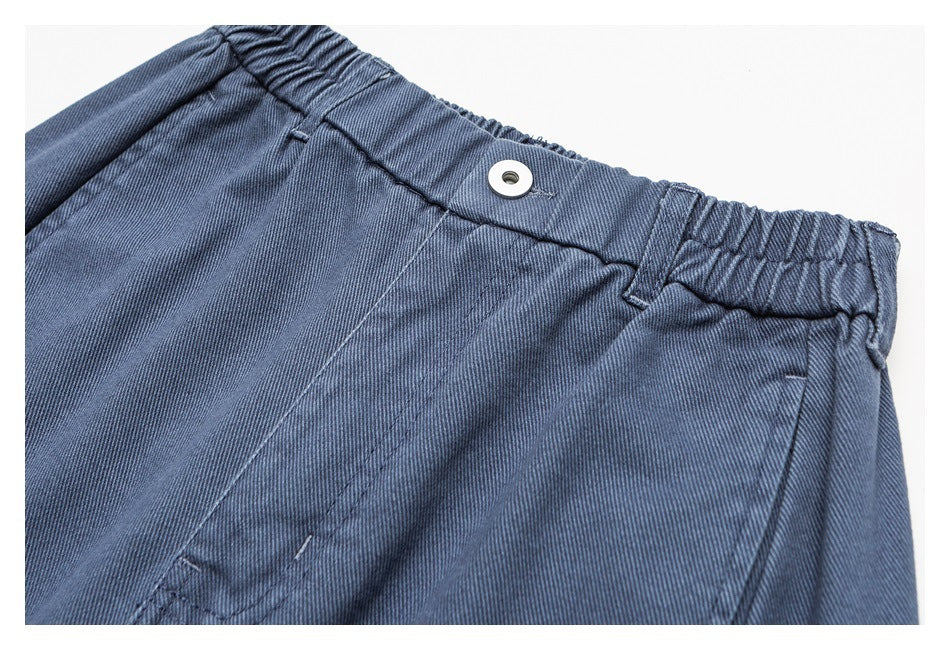 Close-up of the blue pants' elasticized waistband, belt loops, button closure, and front stitching.