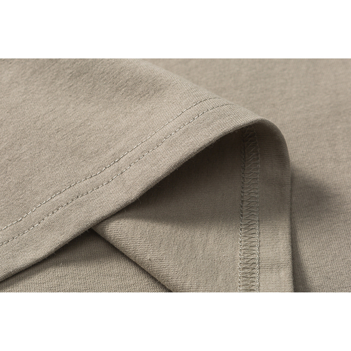 Close-up of taupe T-shirt fabric showing a folded hem, double stitching, and an overlocked seam.