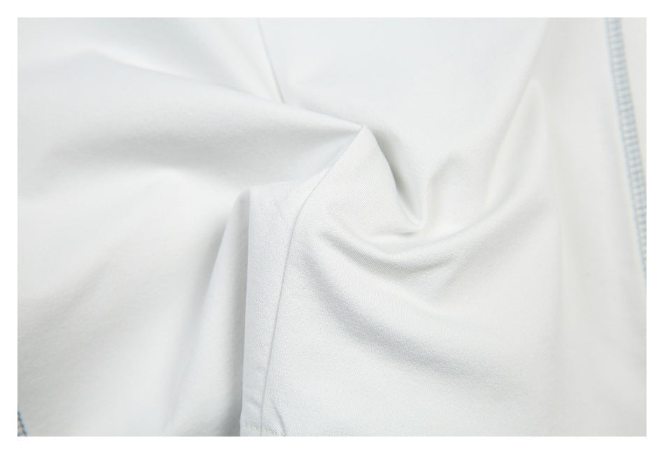 Close-up of softly draped white garment fabric with a narrow seam and pale blue stitching at the edge.