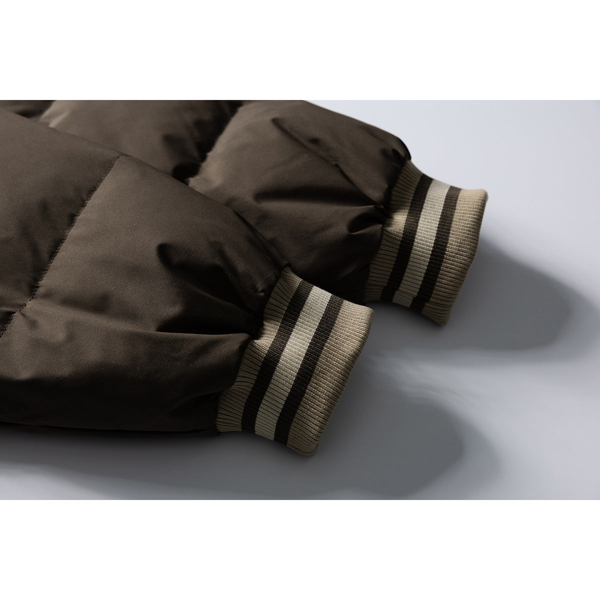 Close-up of a dark brown padded jacket's gathered sleeves and striped rib-knit cuffs.