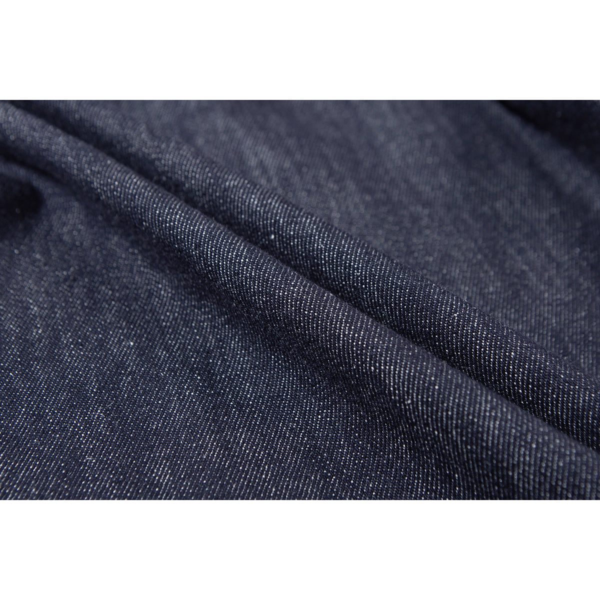 Macro view of dark indigo denim folded to show its diagonal weave and texture.