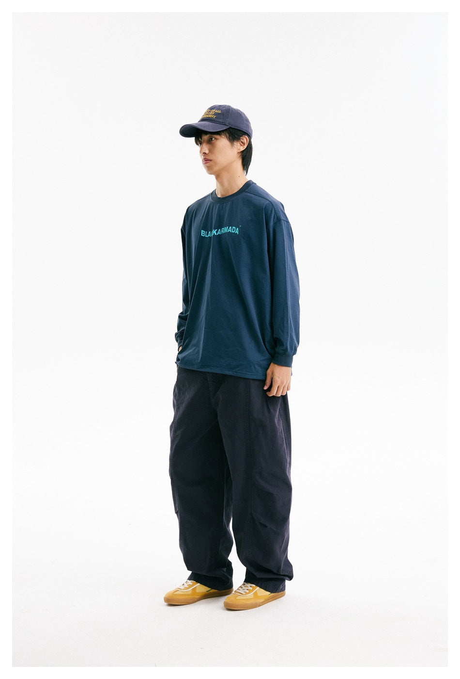 Three-quarter view of a model in a navy long-sleeve shirt with cyan chest lettering and loose dark pants.