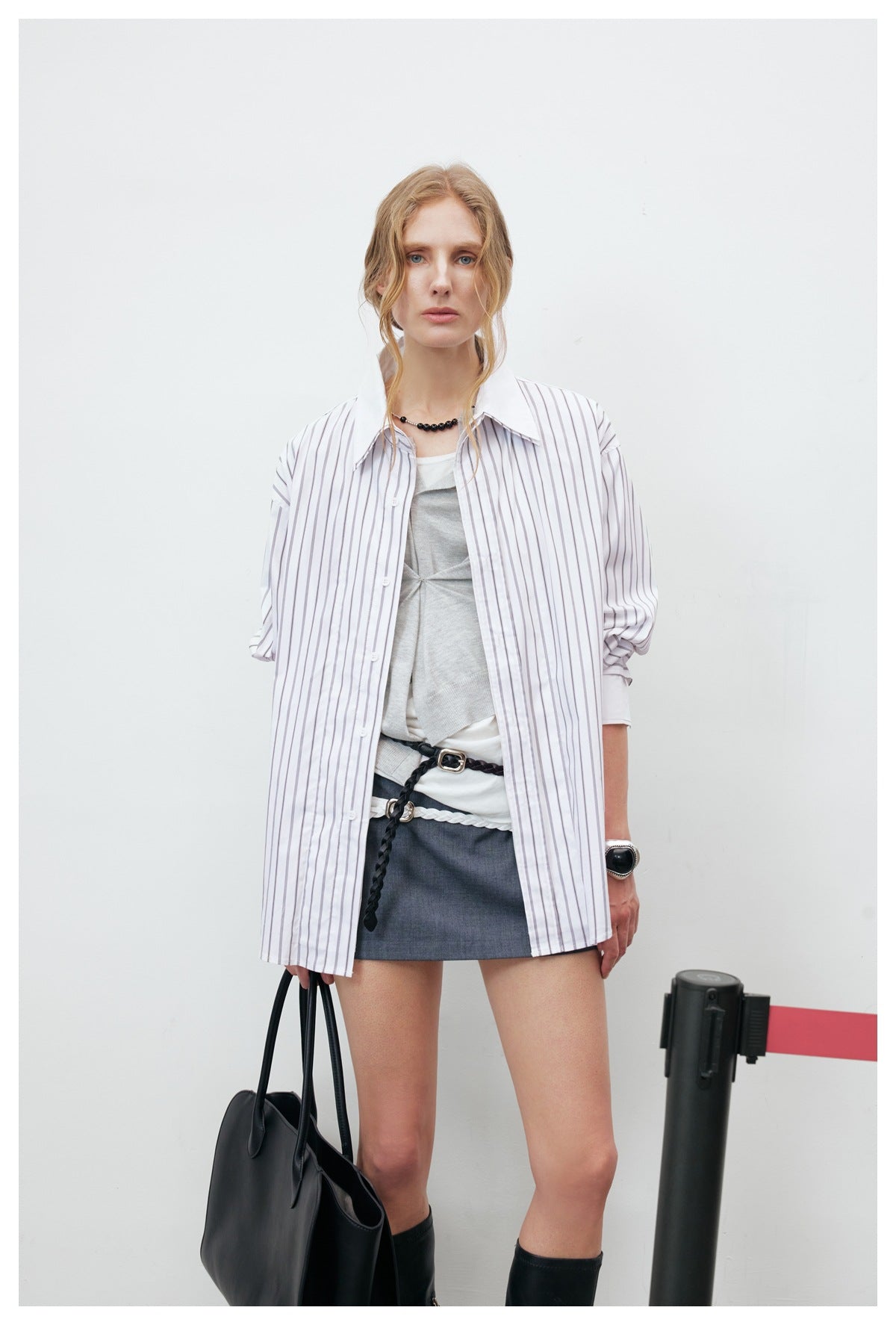 Front view of a model wearing a loose white shirt with dark vertical stripes over a gray top and short skirt.