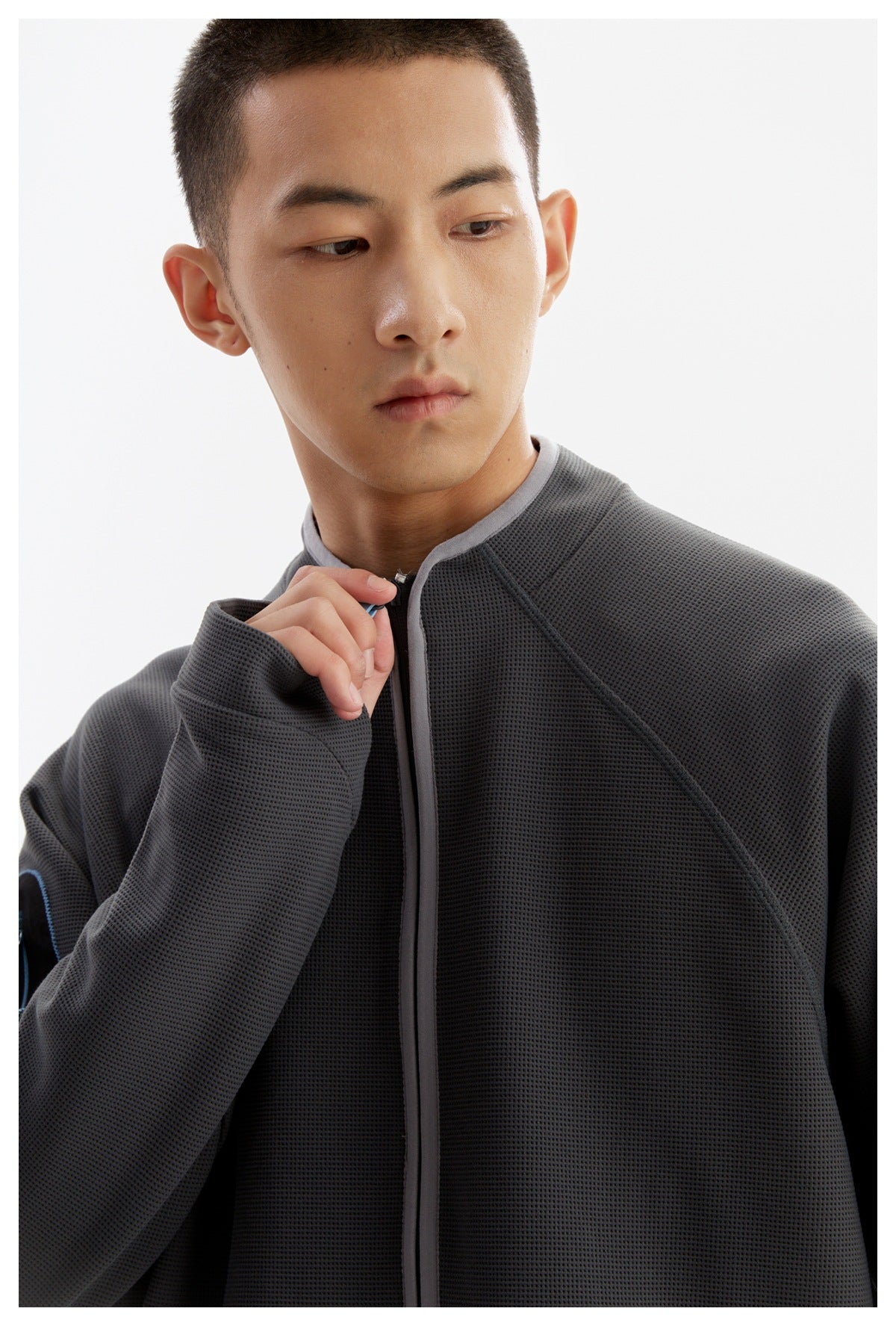 Close view of a man wearing a textured charcoal jacket with a stand collar and front zipper.