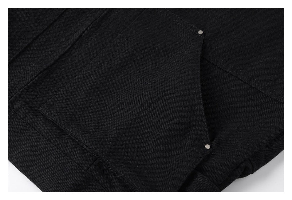 Close-up of a black garment pocket flap with two small metal snaps and visible stitching.
