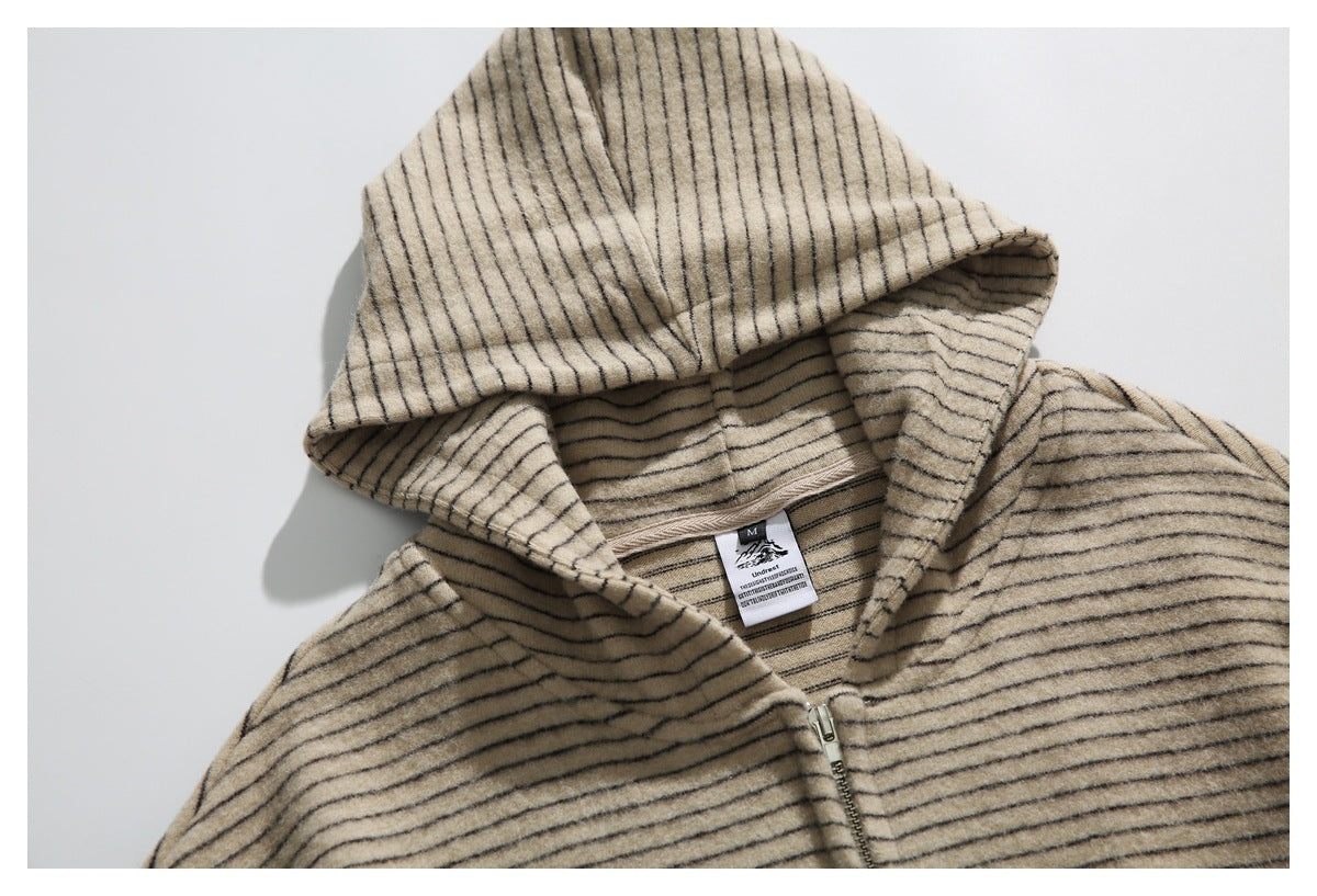 Close view of a beige hooded zip-up garment with thin dark stripes and its neck label.