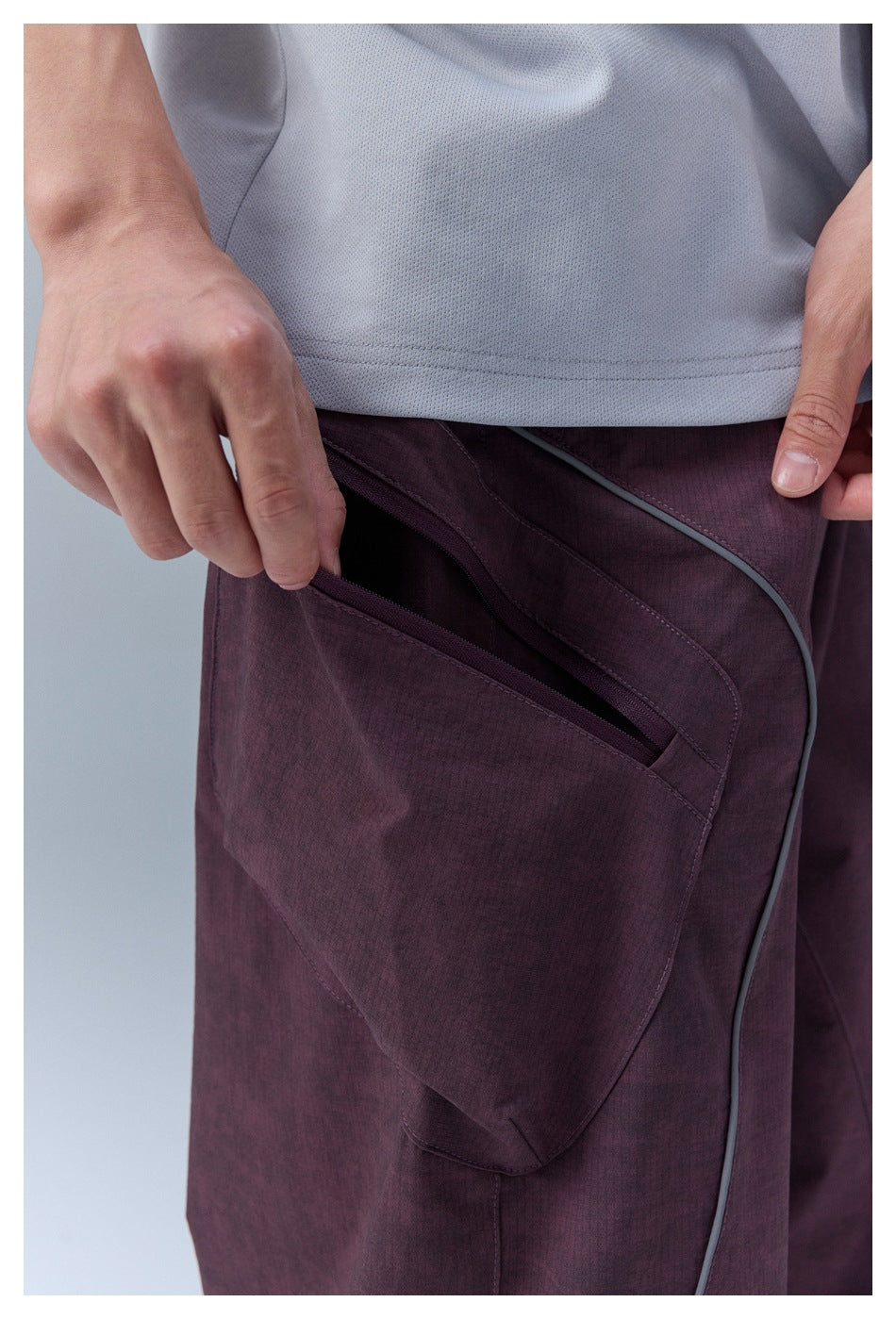 Close-up of a plum cargo-pants pocket with a zipper, shown beneath a light gray shirt.