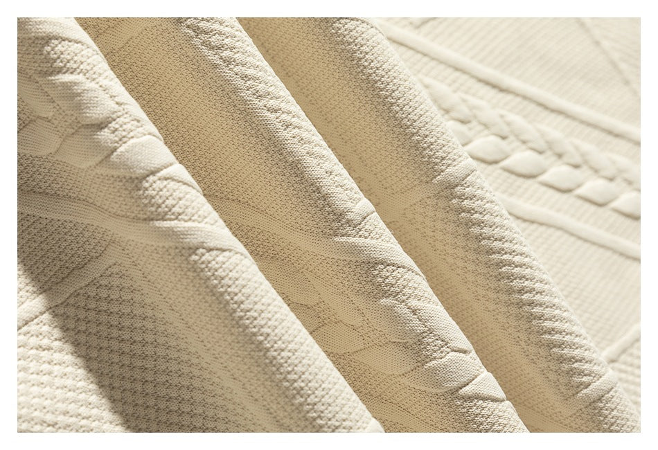 Close-up of warm ivory knit fabric with raised cable and geometric patterns.