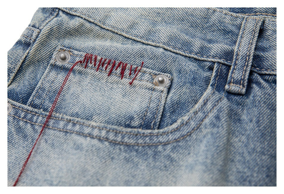 Close-up of the small front coin pocket, metal rivets and red thread detail on faded blue jeans.