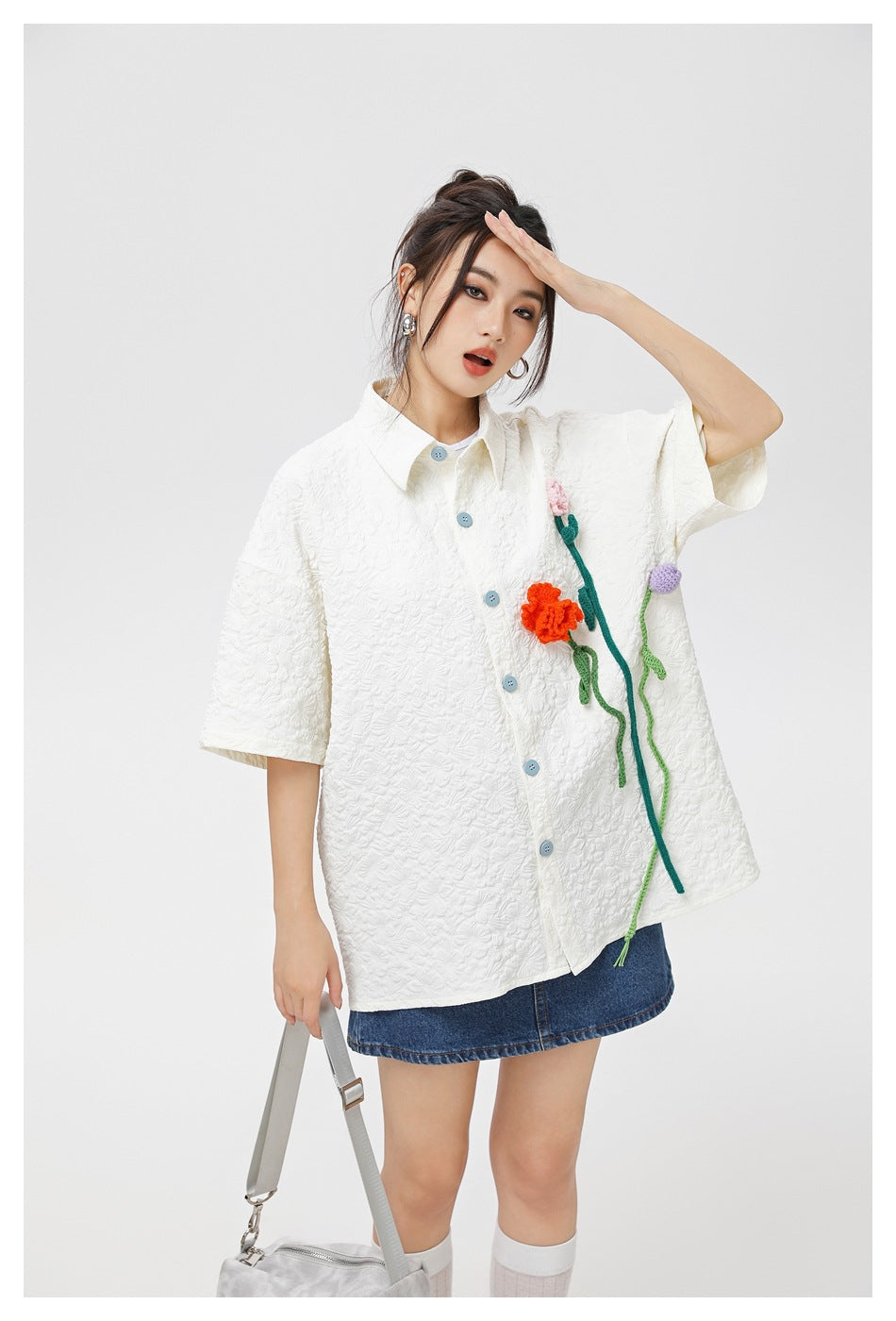 Closer view of a model wearing a white textured shirt with blue buttons and colorful flower appliqués.