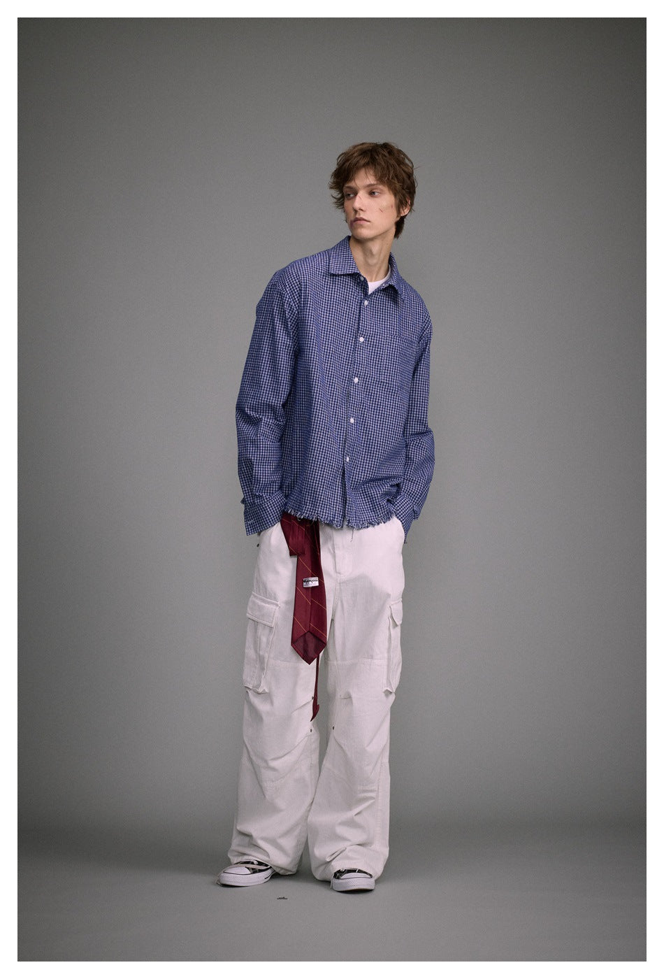 Model in a blue check frayed-hem shirt and white cargo pants, turned slightly to the side with hands in pockets
