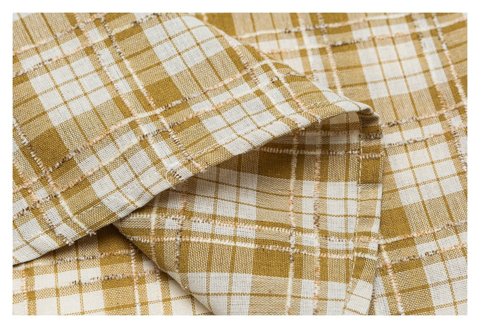 Close-up of folded mustard and cream plaid fabric with visible seams and stitched edges.