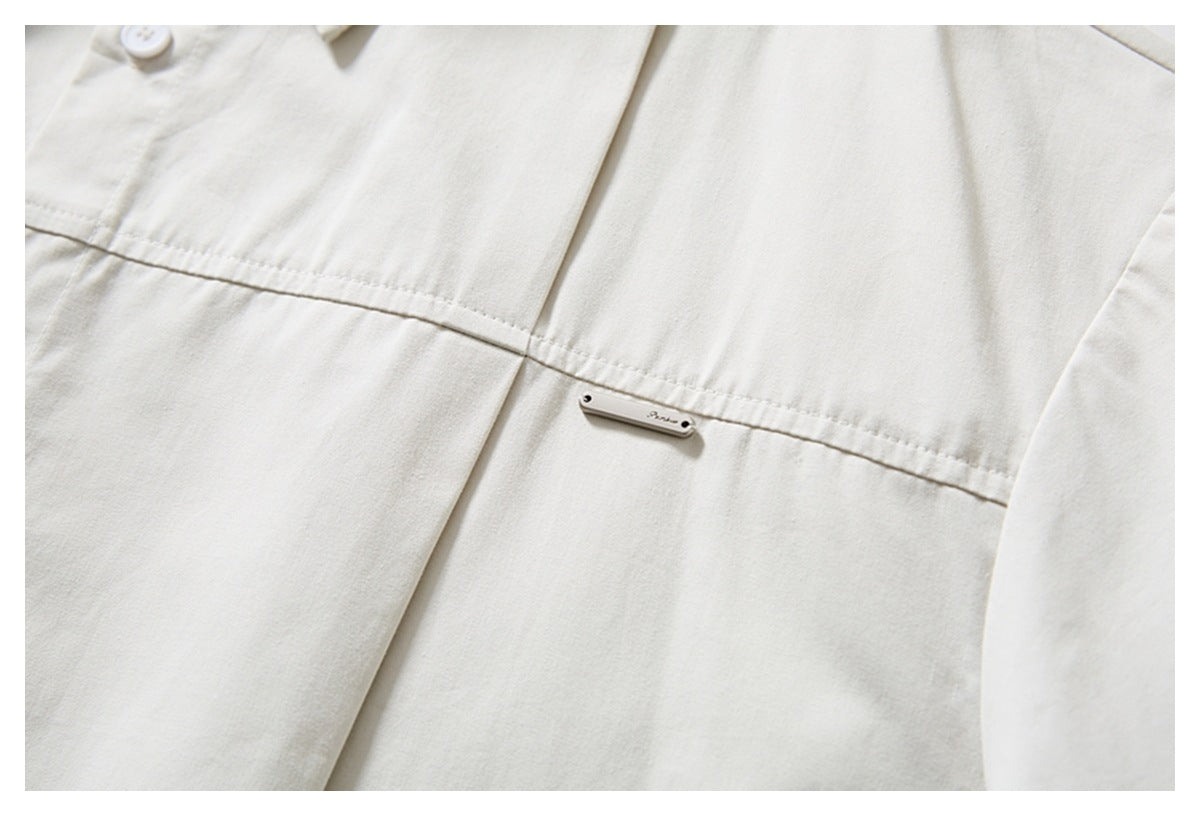 Close-up of an ivory shirt with a horizontal seam and a small metal logo plaque.