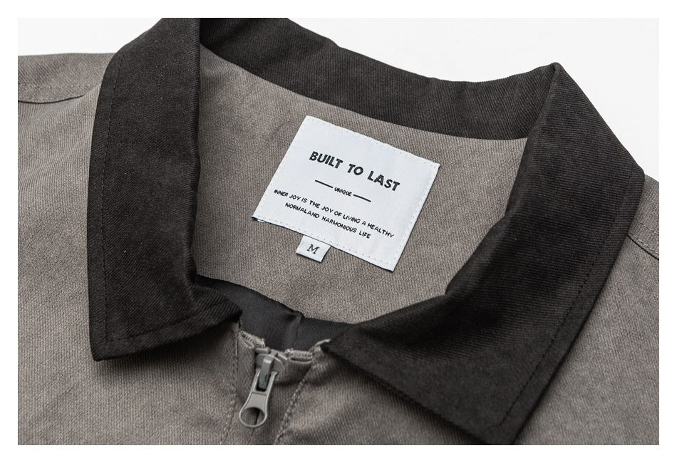 Close-up of a gray jacket’s dark collar, front zipper, and white neck label reading “BUILT TO LAST.”