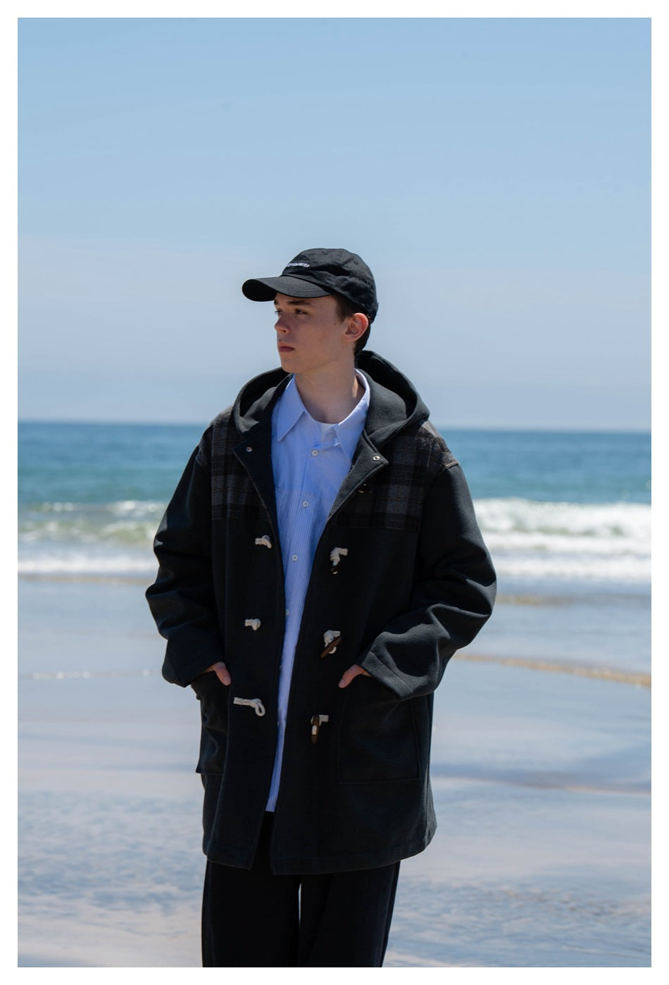 Front view of a person wearing an open dark hooded duffle coat with plaid shoulder panels and toggle closures.