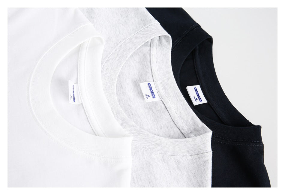 Close-up of crew necklines and inner labels on white, light heather-gray, and black T-shirts.