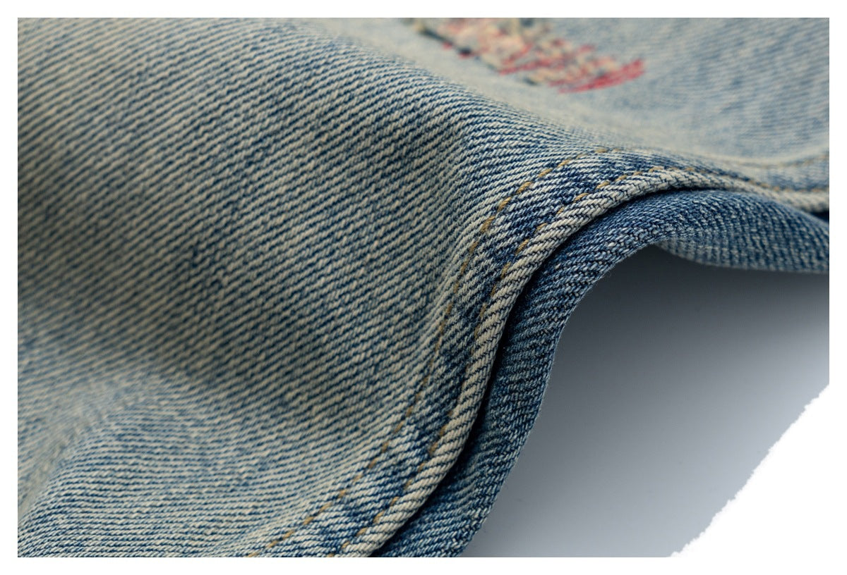 Close-up of light blue denim with a folded edge, golden stitching, and faint blurred red print.