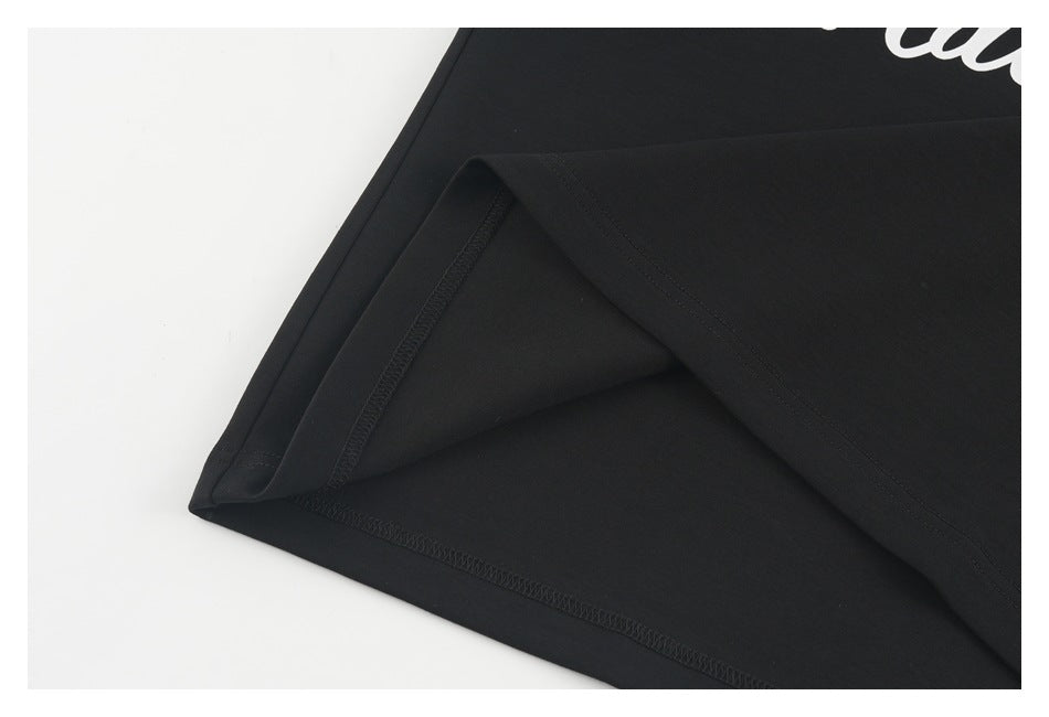 Close-up of a black garment's folded hem and stitching, with a small cropped portion of white print at the edge.