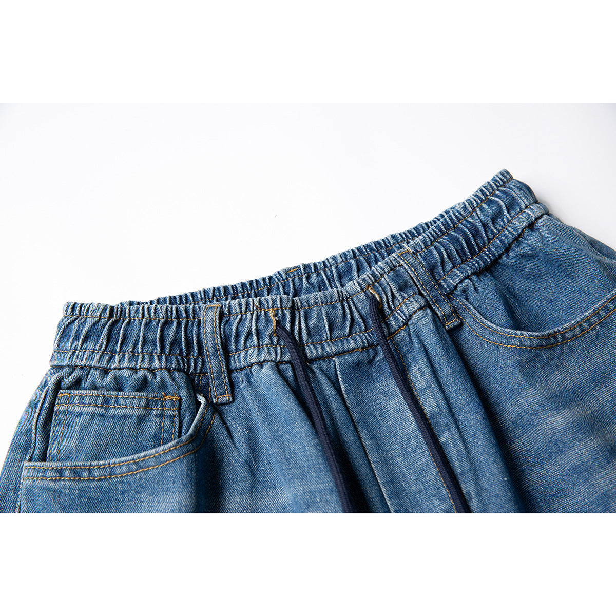 Close-up of blue denim pants showing an elastic waistband, belt loops, drawstring, and front pockets.