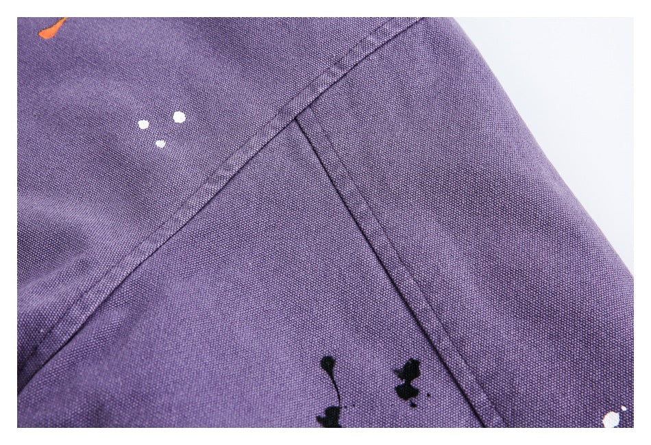Close-up of purple jacket fabric and seams with scattered white, orange, and black paint-like marks.