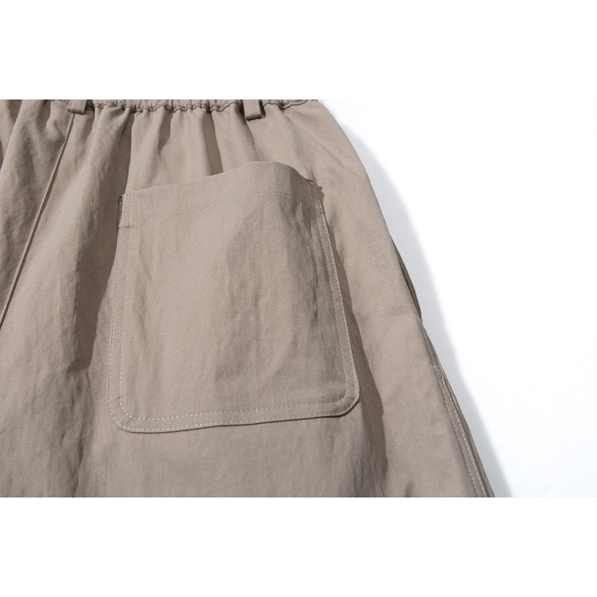 Close-up of taupe shorts showing a large stitched patch pocket and part of the gathered waistband.
